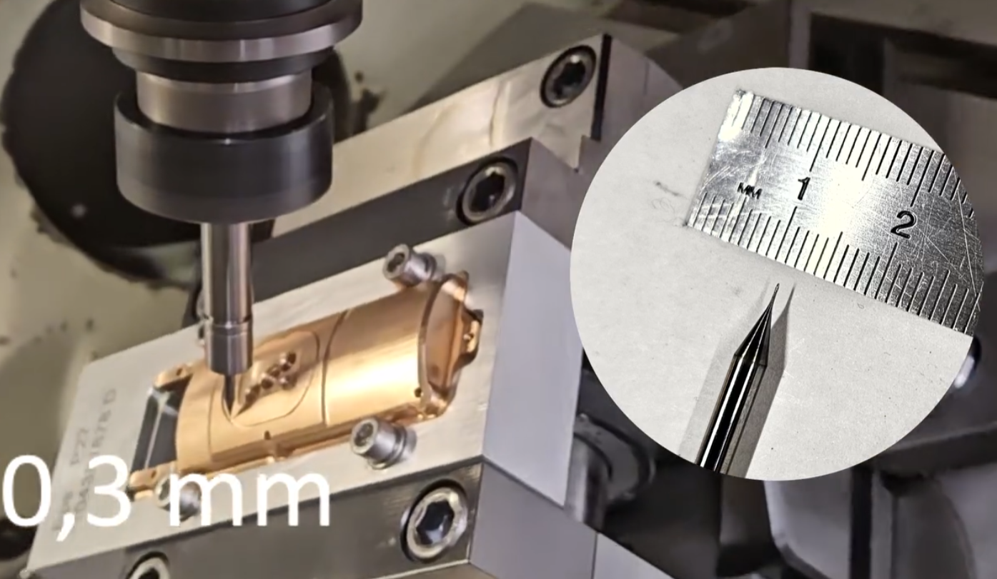 Image illustrant un processus d'usinage de précision, montrant une machine travaillant sur une petite pièce métallique avec une extrême précision. Au premier plan, on peut voir un outil de coupe en train de réaliser des détails fins sur une pièce en métal. En insert, une règle montre la taille minuscule d'un autre outil de coupe, mesurant moins de 1 millimètre. Le texte "0,3 mm" est affiché en bas à gauche, soulignant la précision de l'usinage.