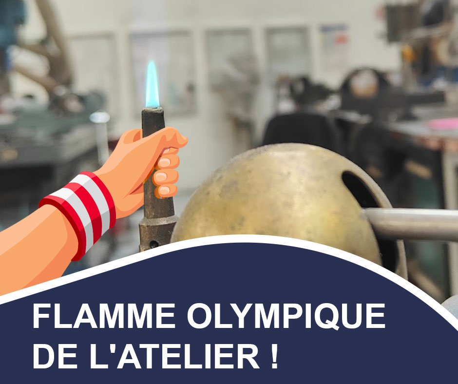 Image montrant une main stylisée tenant un chalumeau avec une flamme bleue, symbolisant la "Flamme Olympique de l'Atelier". L'arrière-plan flou suggère un environnement d'atelier ou de fabrication, avec divers outils et équipements visibles. Le texte "FLAMME OLYMPIQUE DE L'ATELIER !" est affiché en bas de l'image sur un fond bleu foncé avec une bordure blanche.
