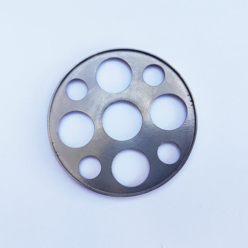 Disque métallique circulaire en acier inoxydable, découpé au laser avec trous de différents diamètres – exemple de pièce usinée par découpe laser de précision.