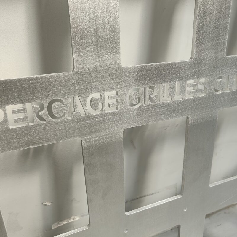 Panneau métallique avec lettrage découpé au laser « PERCAGE GRILLES CLIM » – plaque en aluminium brossé usinée par découpe laser pour grilles de ventilation climatisation.
