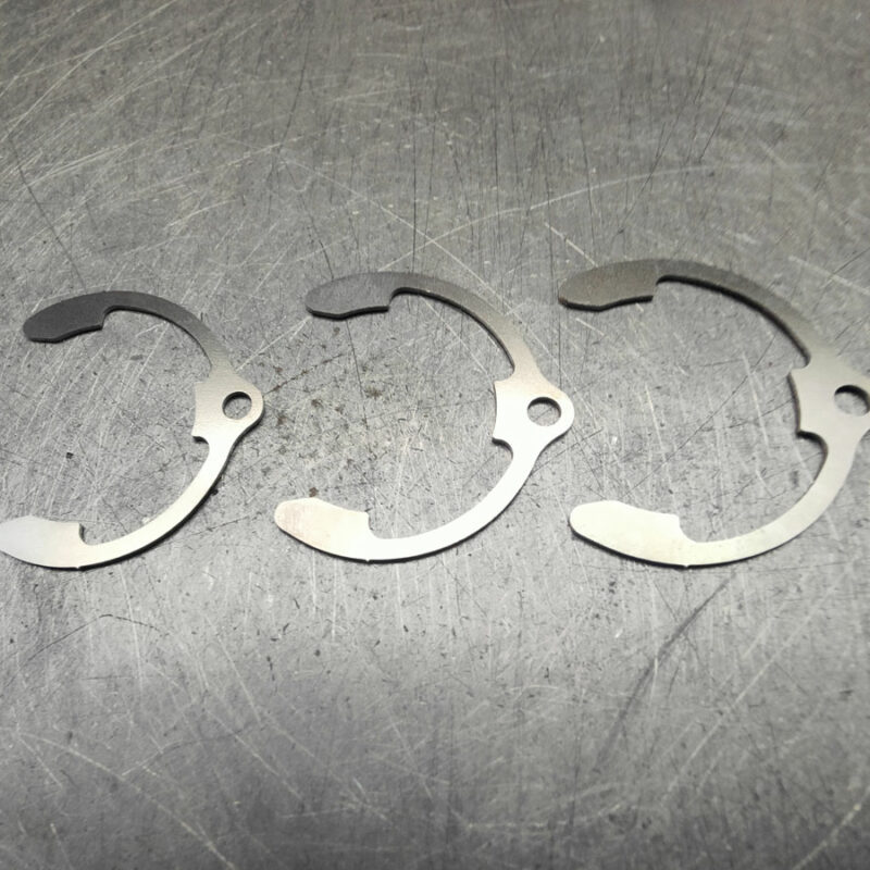 Pièces métalliques en forme de demi-lune découpées au laser – composants de précision en acier inoxydable sur table d’atelier, issus de découpe laser fine pour l’industrie mécanique. Circlips.
