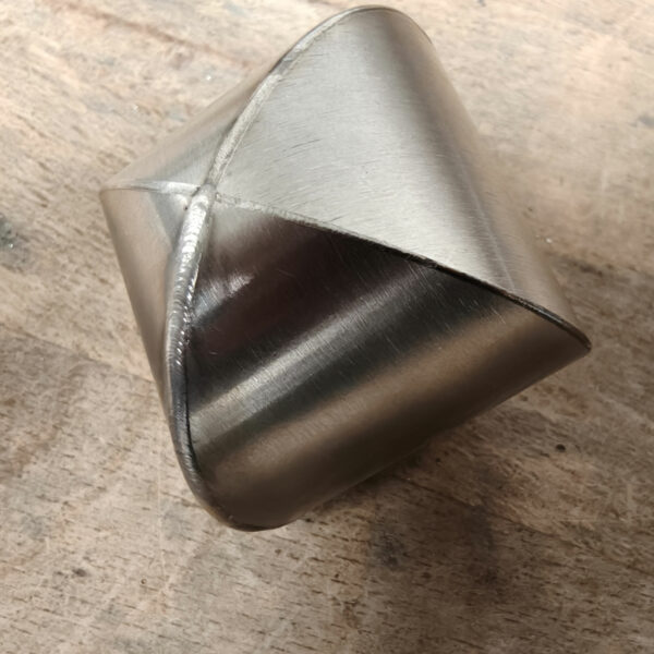 Pièce métallique formée et soudée, présentant une jonction propre typique d’une soudure laser. La surface est lisse avec des reflets thermiques visibles, posée sur un établi en atelier.